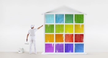rear view of painter man pointing with finger the colors house model on wall, with paint roller and bucket, isolated on white
